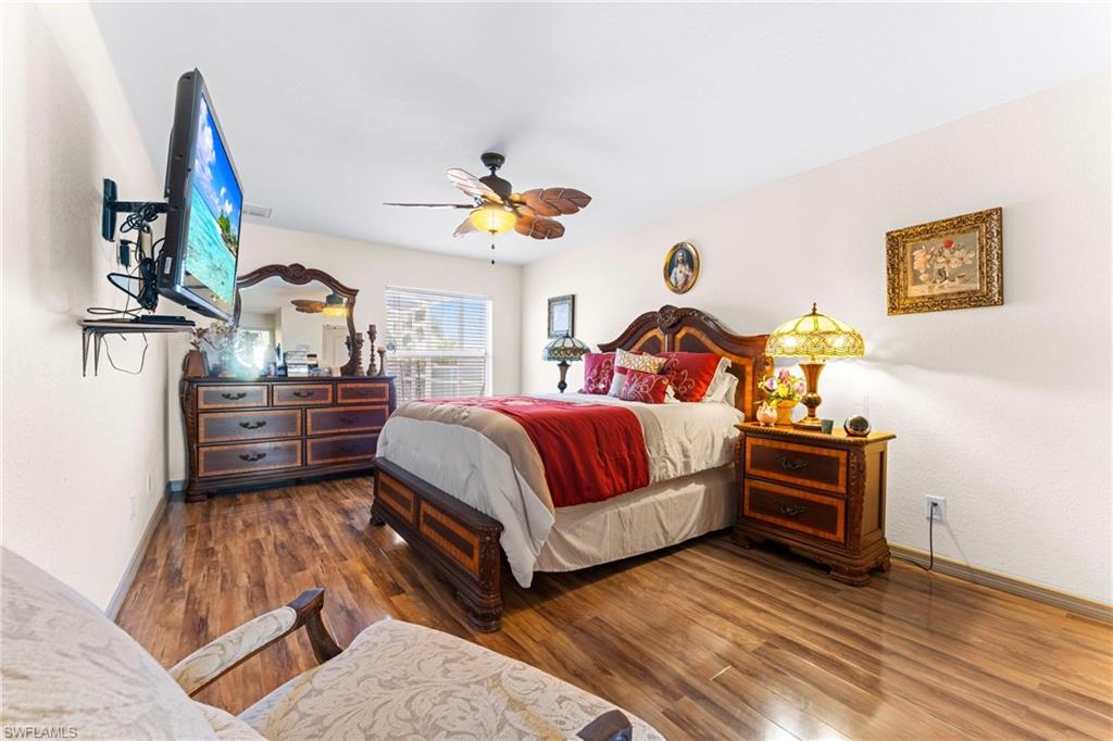 Spacious room featuring wood-finish flooring, a ceiling fan with light fixture, and a large window with blinds