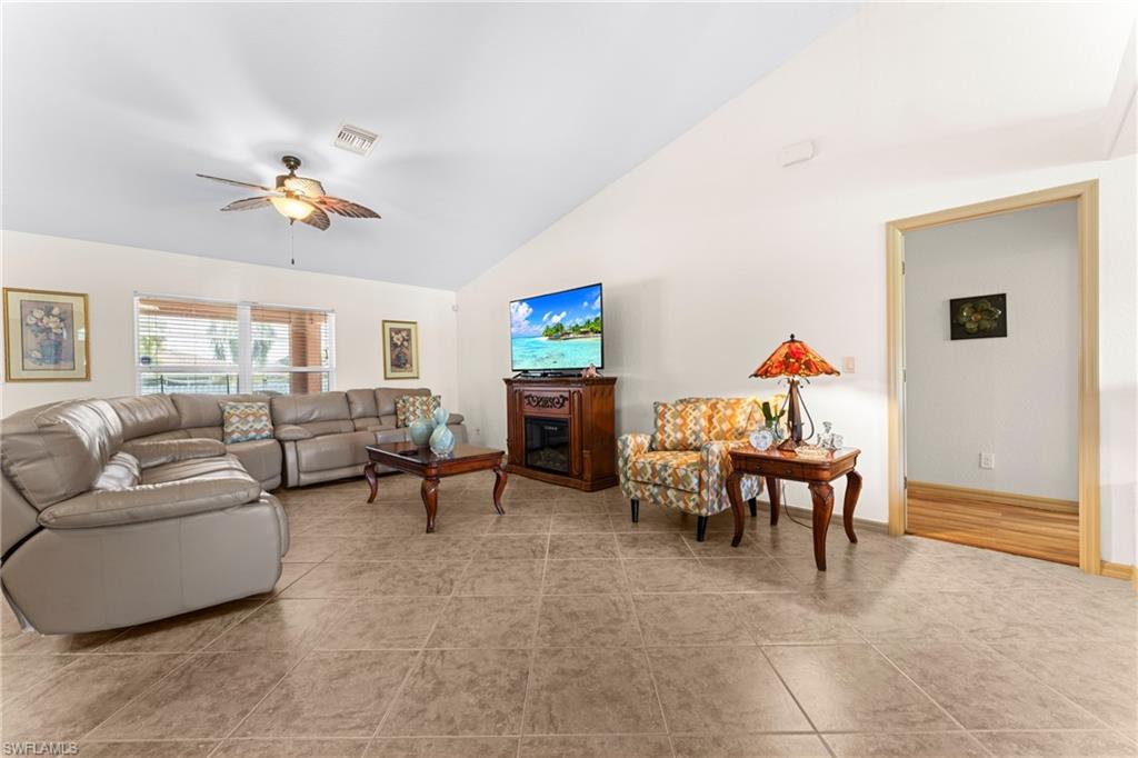 Spacious room featuring vaulted ceilings, neutral-toned tile flooring, a ceiling fan with integrated lighting, a large window, and an open doorway with wood trim