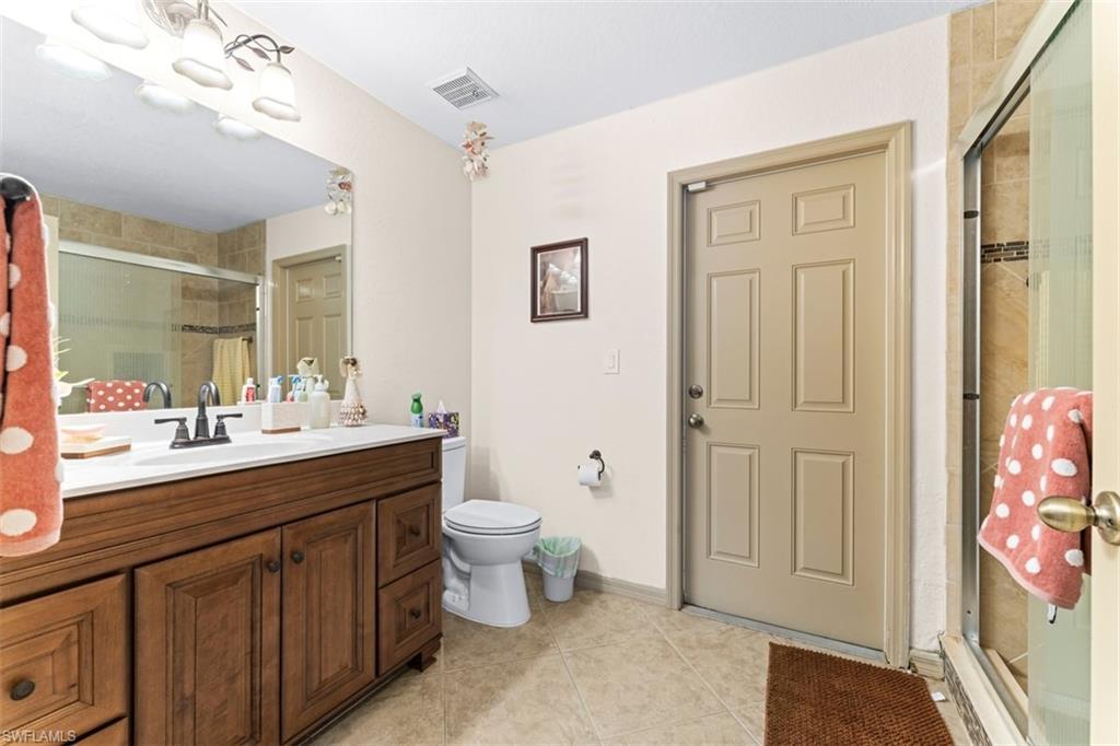 Bathroom featuring a dark wood-finish vanity with a white countertop and rectangular sink, a glass-enclosed shower with tiled walls and decorative accent band, and tiled flooring