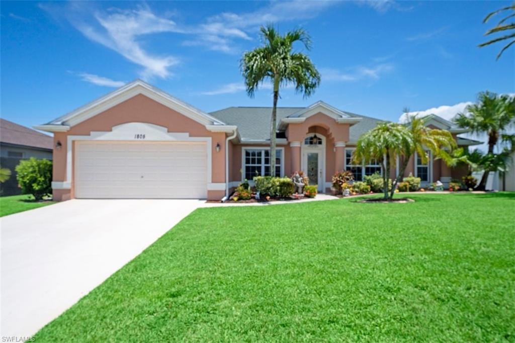 Stucco exterior with a peaked roofline, an attached two-car garage, a concrete driveway, and mature palm trees