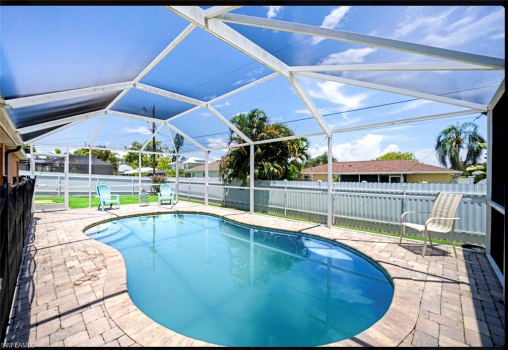 Enclosed screened patio featuring a freeform swimming pool, paver deck, and a white perimeter fence