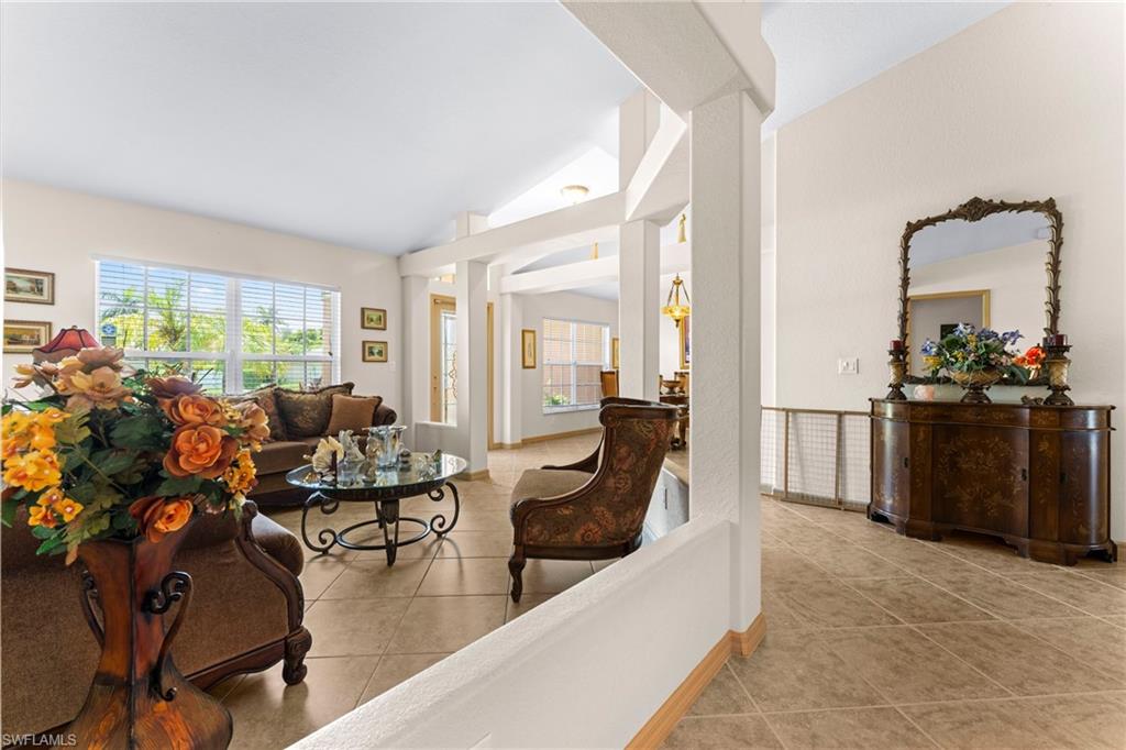 Spacious living area featuring vaulted ceilings, tile flooring, large windows with blinds, and architectural columns