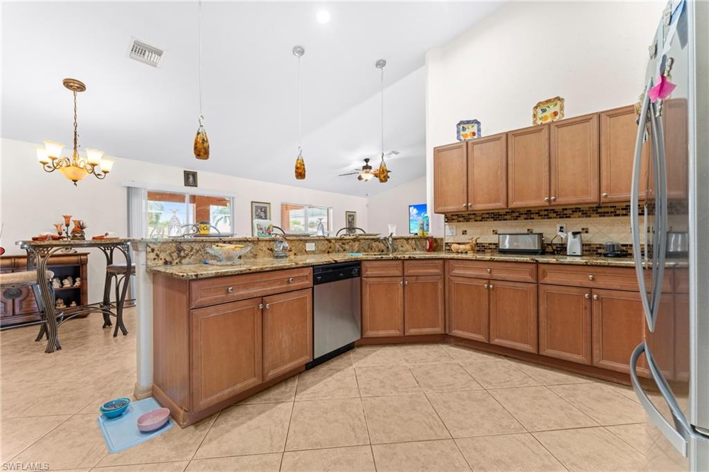 Spacious kitchen featuring light wood cabinetry, stone countertops, a tile backsplash, and stainless steel appliances