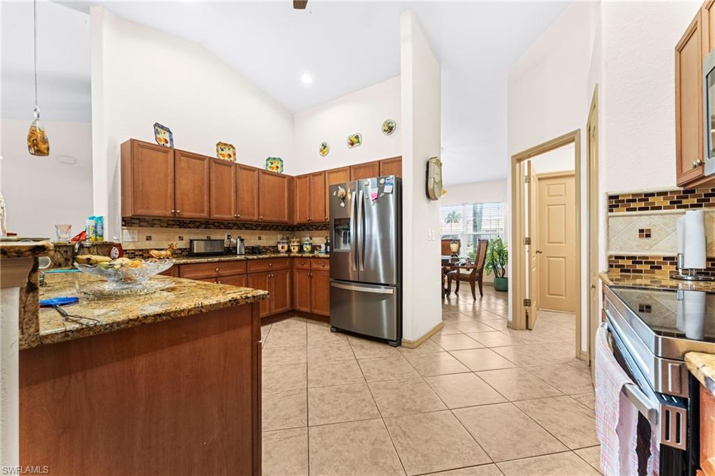 Kitchen featuring wood cabinetry, stainless steel refrigerator, granite countertops, tile backsplash, and tile flooring