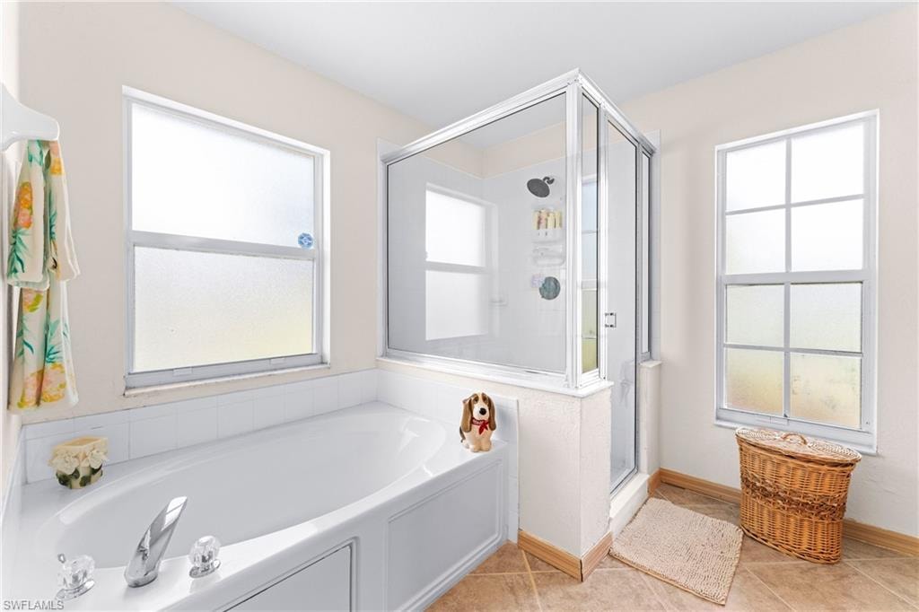 Deep soaking tub with chrome fixtures, enclosed shower with glass surround, and tile flooring