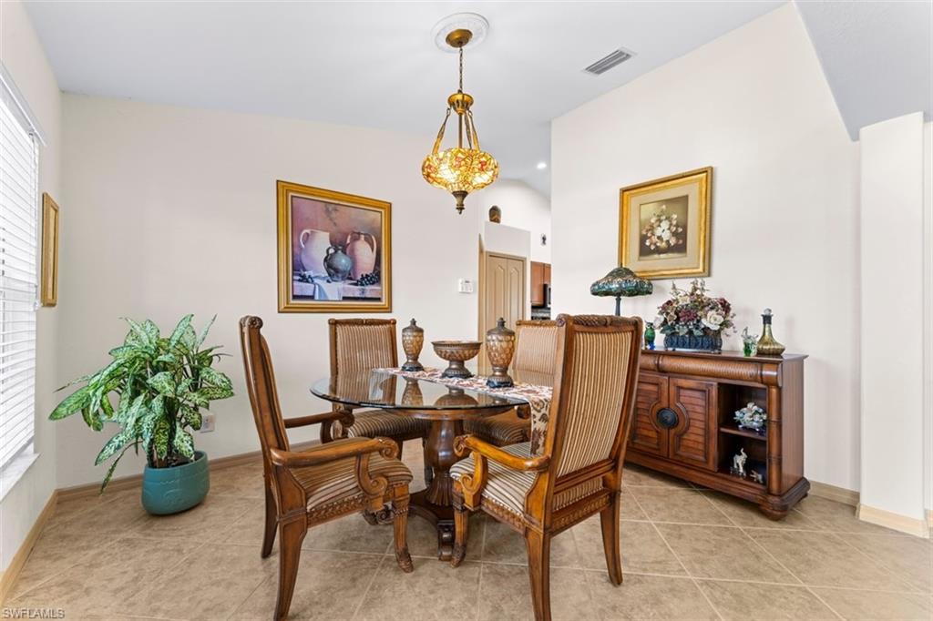 Dining area featuring neutral wall tones, tile flooring, a glass-top table, and a decorative overhead light fixture