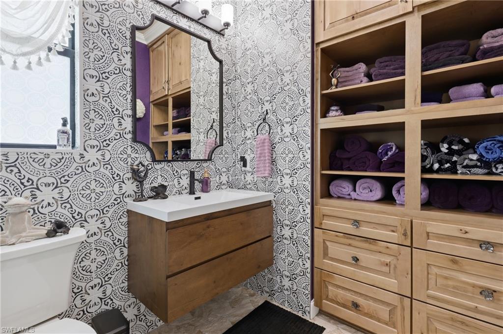 Cabana Bathroom featuring patterned wall tiling, a floating wood-finish vanity with a white countertop and a matte black faucet, and a decorative framed mirror with integrated lighting