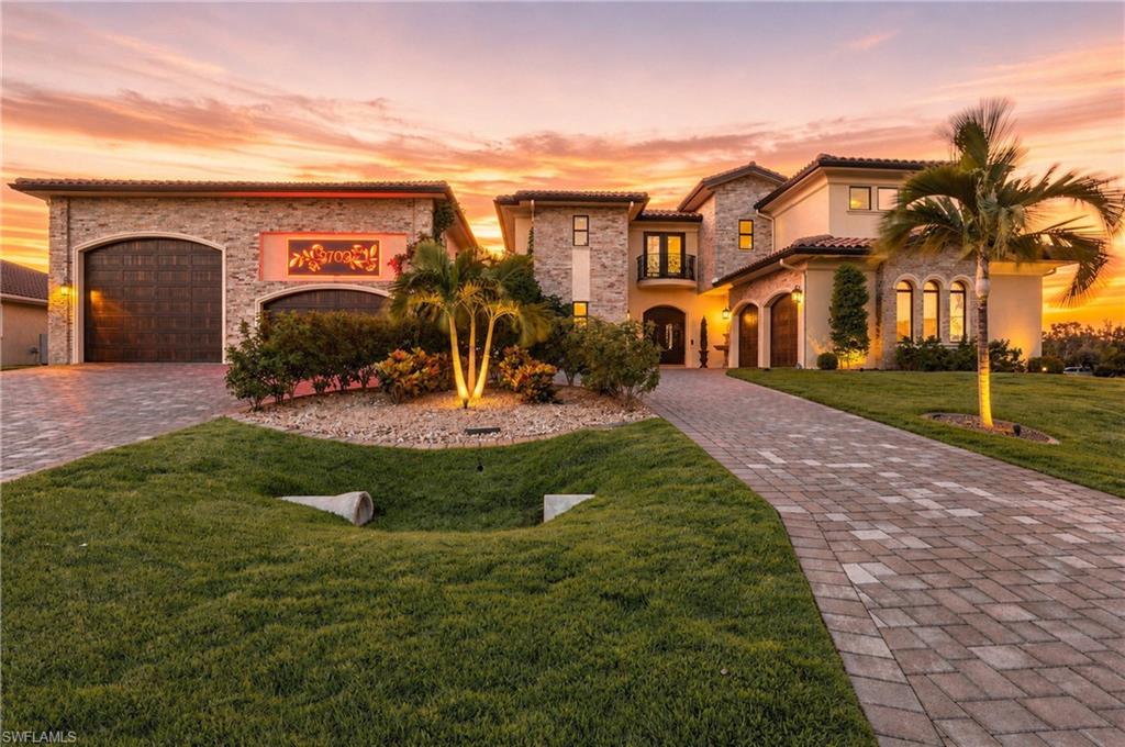 Expansive circular paver driveway leading to a multi-car garage and main entrance and mature landscaping