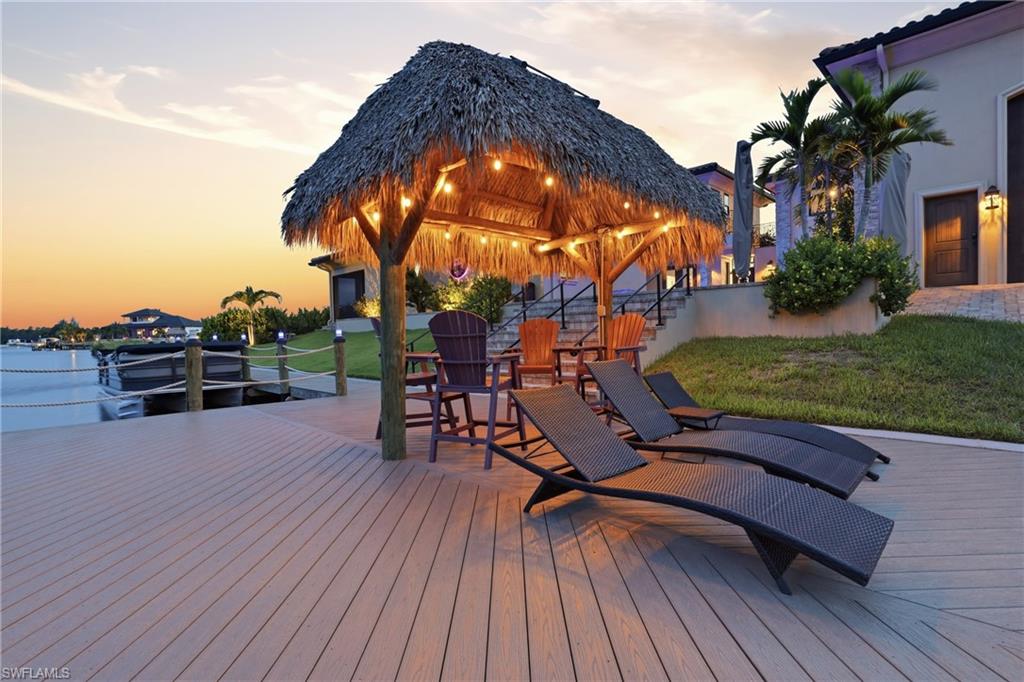 Waterfront decking with a thatched-roof tiki hut, string lighting, and direct water access with a dock
