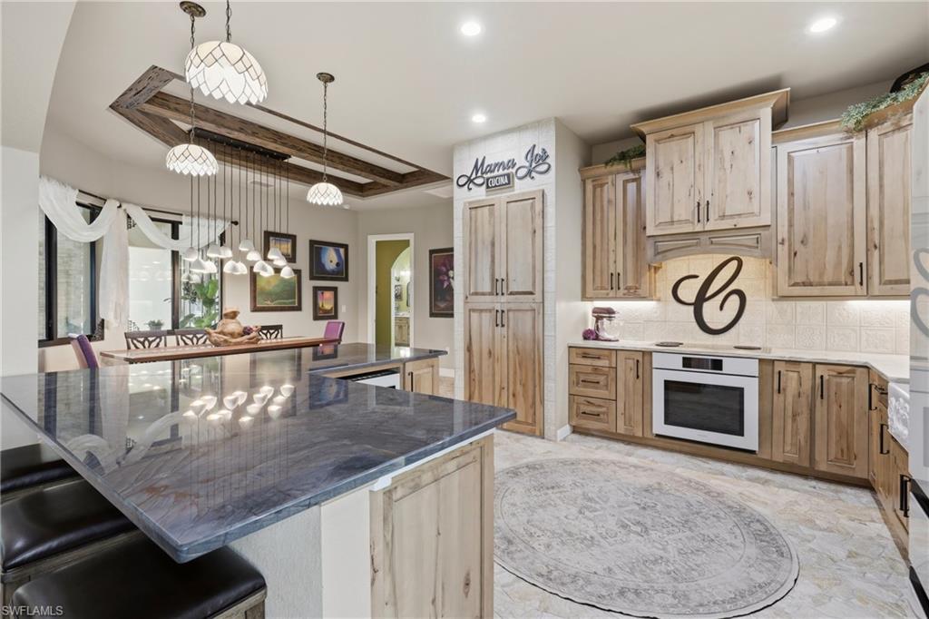 Spacious kitchen featuring an expansive island with a polished countertop, light wood cabinetry, built-in oven, tile backsplash, and recessed lighting