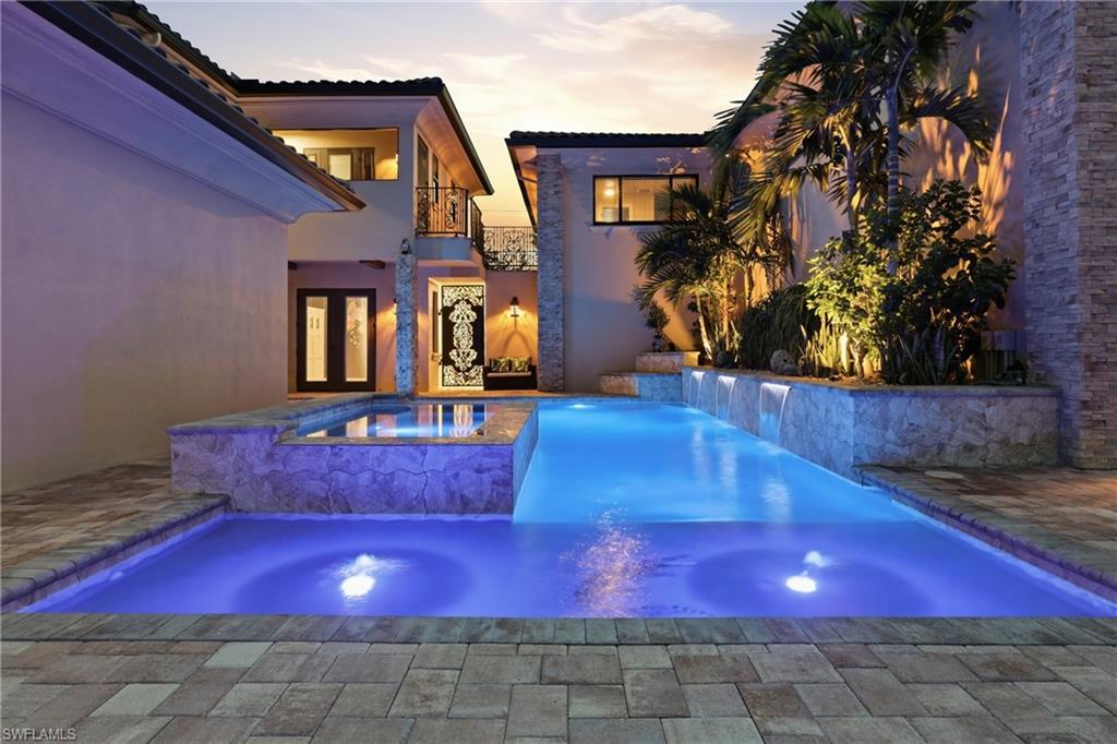 Resort-style pool area featuring a rectangular main pool with integrated spa, illuminated water features, and a stacked stone accent wall