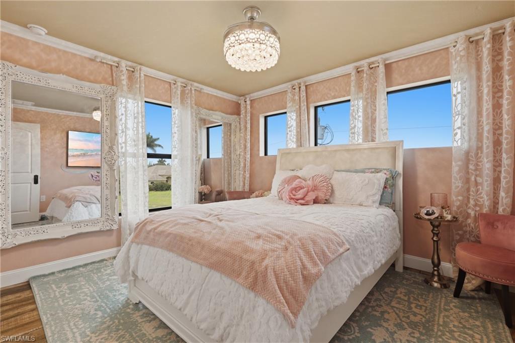 Bedroom featuring four windows with exterior landscape, a detailed crystal chandelier, wood-finish flooring, a white paneled door, and crown molding