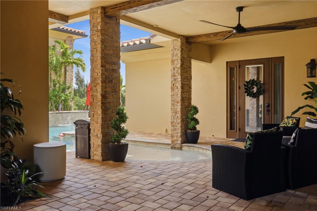 Covered patio with brick paver flooring, stone-clad columns, and exposed beam ceiling