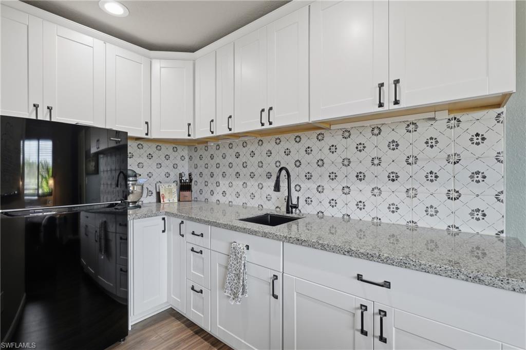 Kitchen featuring white shaker cabinetry with matte black hardware, light-colored granite countertops, and a patterned tile backsplash
