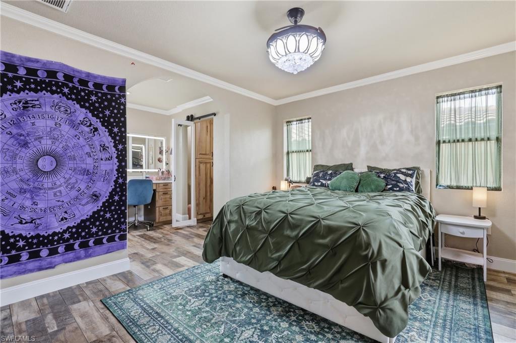 Spacious room featuring wood-finish flooring, crown molding, and two windows with sheer curtains