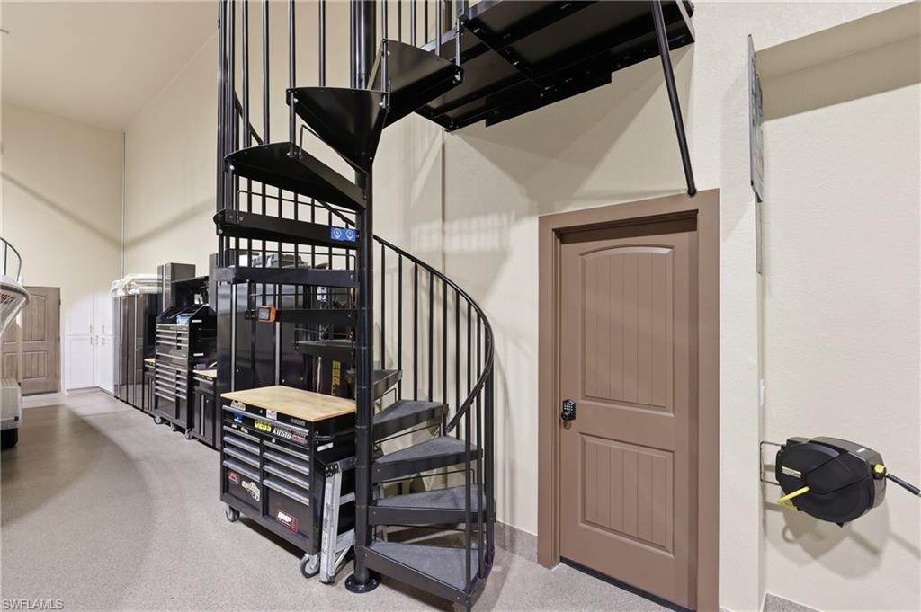 Black metal spiral staircase providing access to an upper level, with light beige walls and a neutral-toned floor