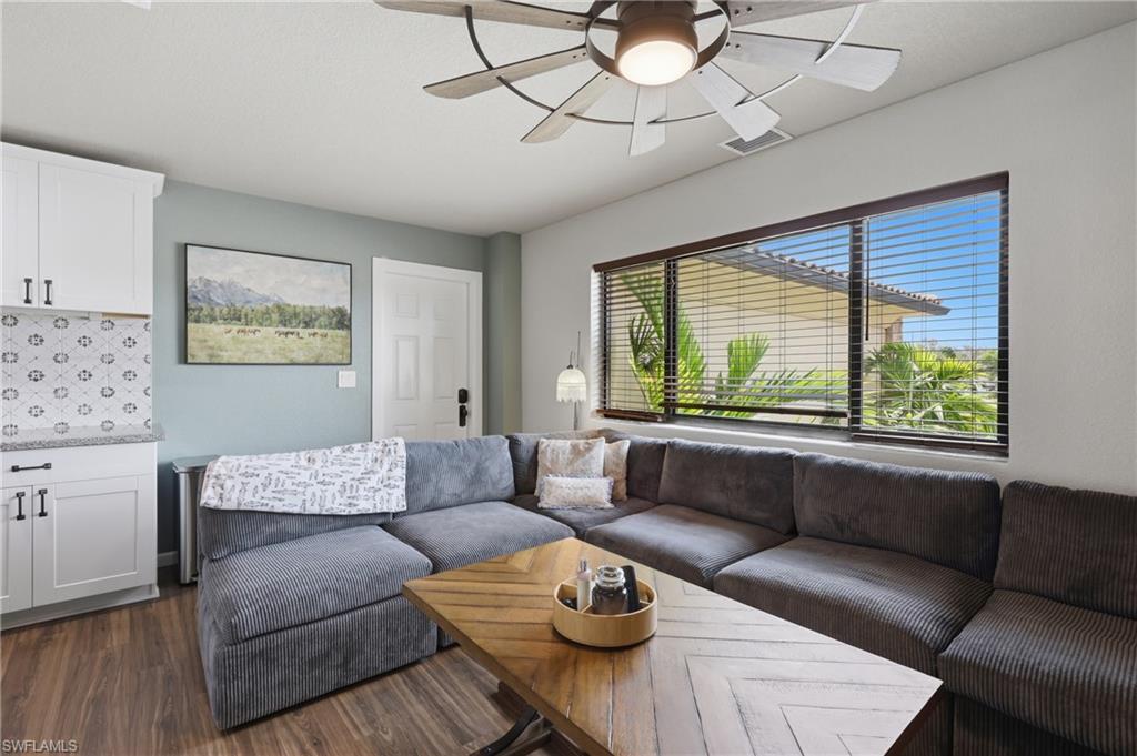 Living area featuring wood-finish flooring, a contemporary ceiling fan, and multiple windows with blinds