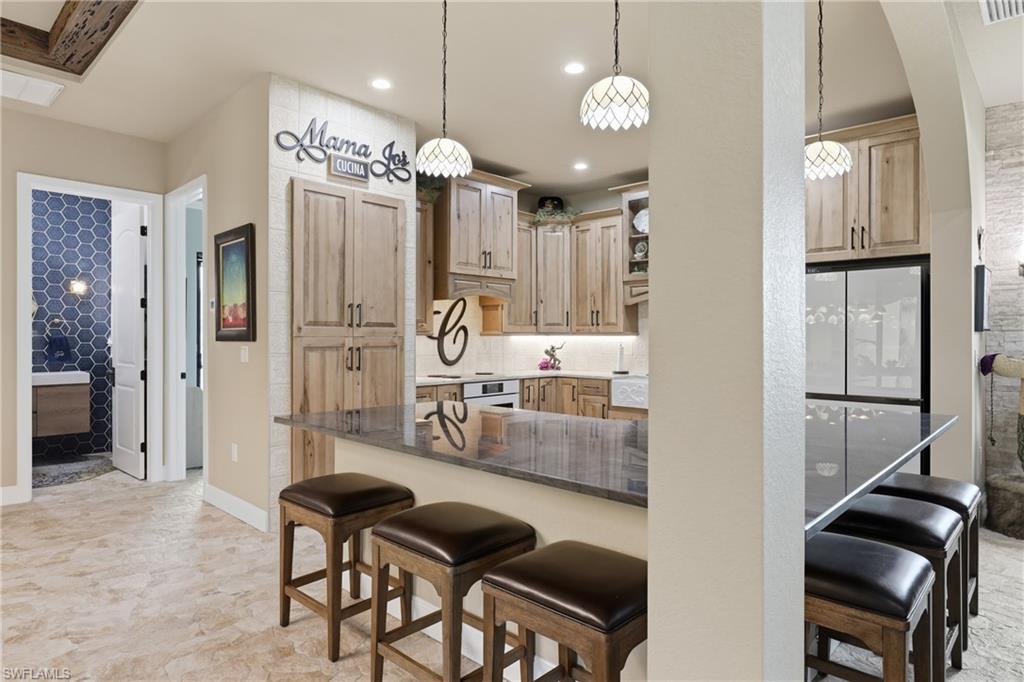 Kitchen featuring wood cabinetry, stone countertops, pendant lighting, and an integrated refrigerator