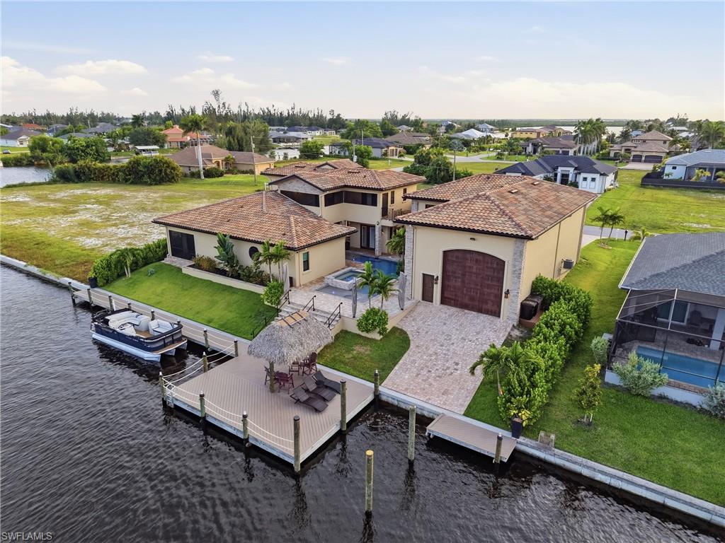 Waterfront property featuring a private boat dock with lift, an expansive paved driveway, and a detached structure with a large archway door