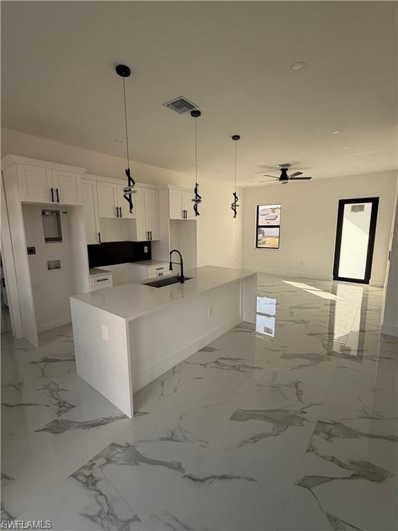 Modern kitchen featuring a waterfall island, white cabinetry, black backsplash, and black pendant lighting