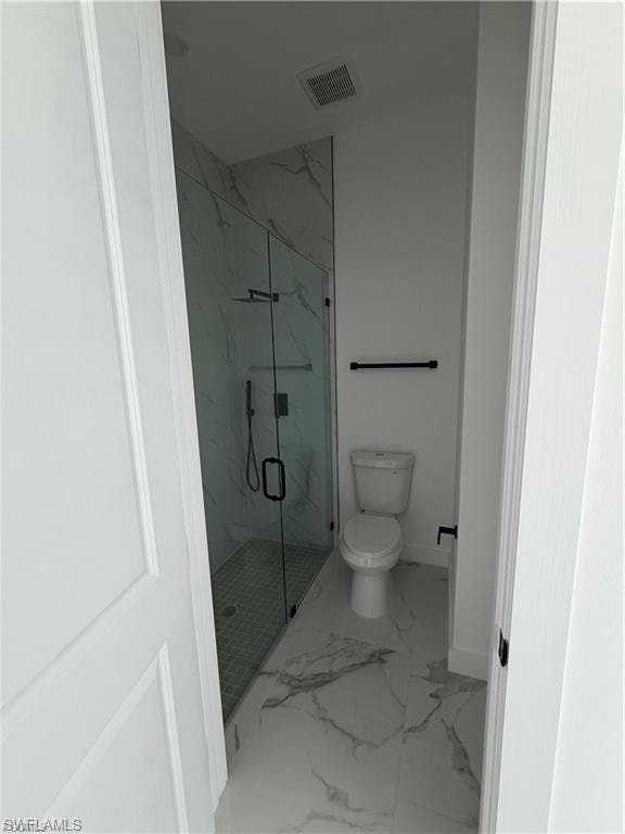 Bathroom featuring a glass-enclosed shower with contrasting floor tile, a wall-mounted towel bar, and a toilet