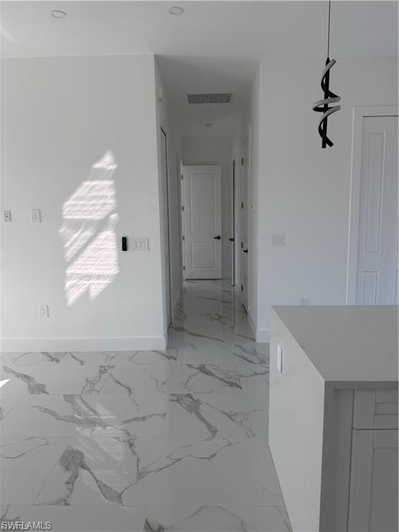 Spacious interior featuring modern tile flooring with a marble-effect pattern, white walls, recessed ceiling lighting, a contemporary pendant light fixture, and an integrated kitchen island with a light-colored countertop