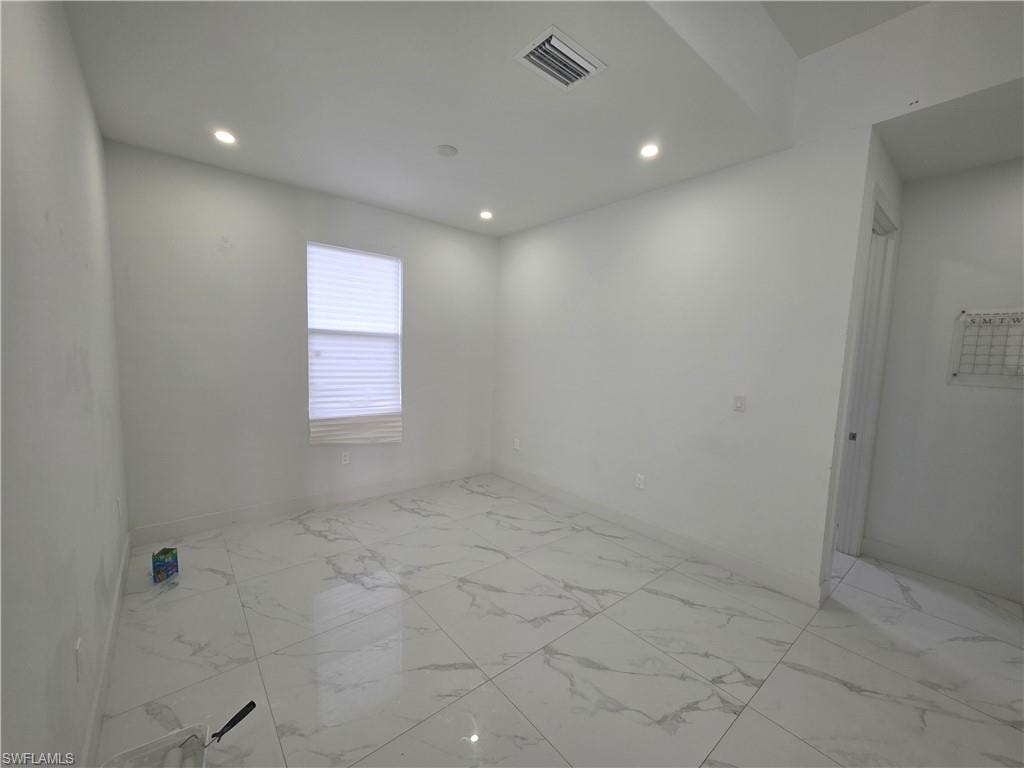 Bright interior room featuring large format tile flooring with subtle veining, recessed ceiling lighting, a window with horizontal blinds, and a white wall finish