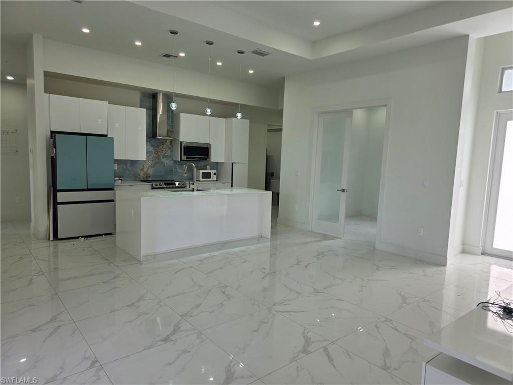 Gourmet kitchen with a waterfall island, sleek white cabinetry, stainless steel appliances, and a striking patterned backsplash