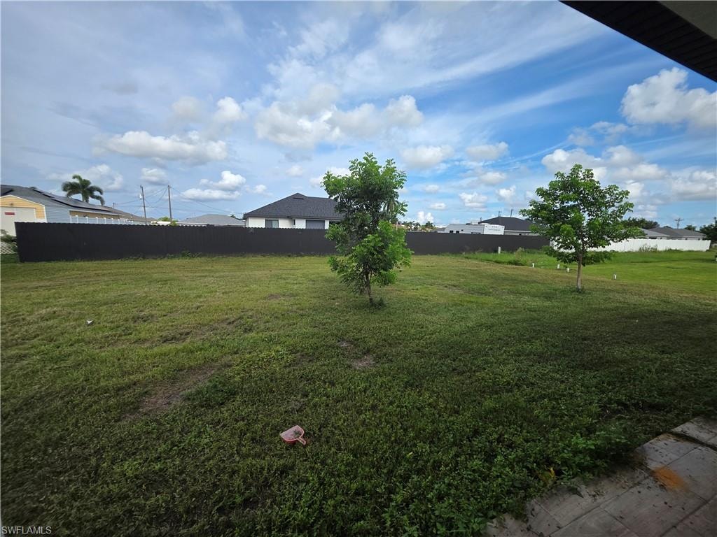 Expansive lot featuring a dark perimeter fence, two young trees, and a spacious green area
