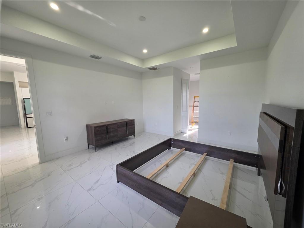 Spacious room featuring large format white tile flooring with gray veining, white walls, and a recessed ceiling with integrated lighting