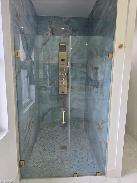 Glass-enclosed shower featuring blue-toned stone walls with natural veining, a patterned floor, recessed shelving, and a gold-finish multi-function shower panel