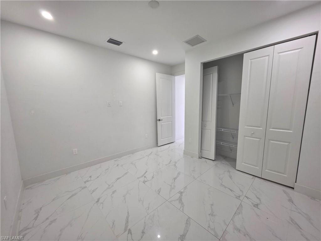 Bright room featuring large format tile flooring with a marble-effect pattern, recessed lighting, white walls, and a bi-fold closet with shelving