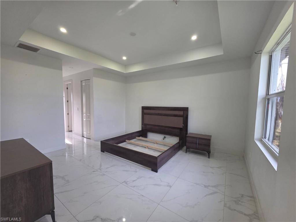 Spacious room featuring large format tile flooring, a tray ceiling with recessed lighting, and a double window for natural illumination