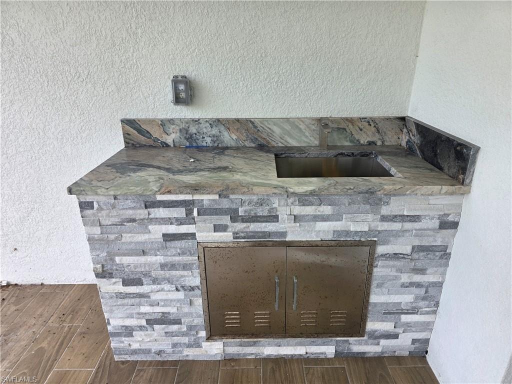 Outdoor kitchen featuring a stone veneer base, patterned countertop, integrated stainless steel sink, and stainless steel cabinet doors