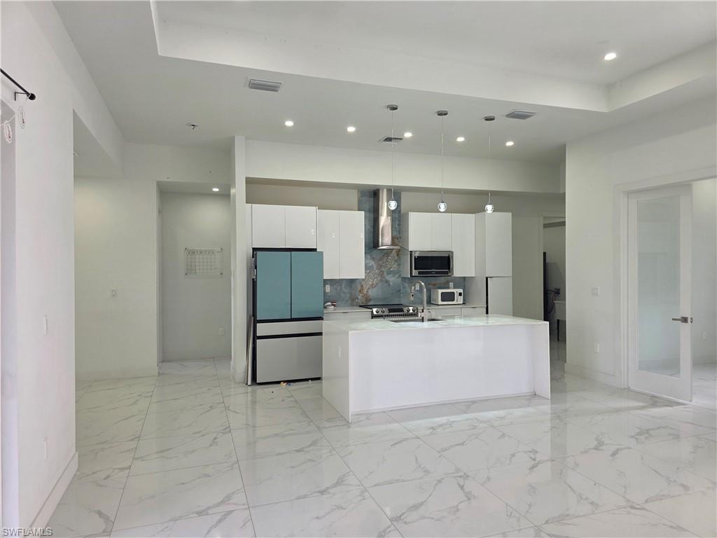 Contemporary kitchen featuring white flat-panel cabinetry, a central island with an integrated sink, and stainless steel appliances