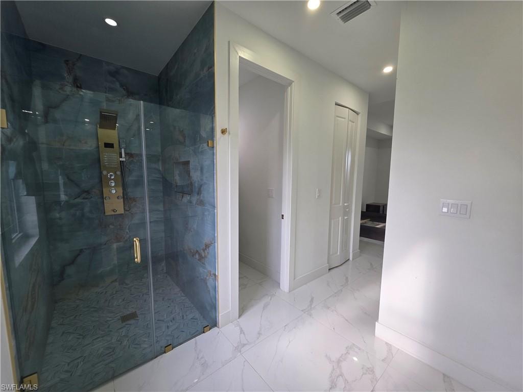 Shower enclosure with blue-toned stone-finish walls, glass door with gold-finish hardware, and a gold-finish shower panel system