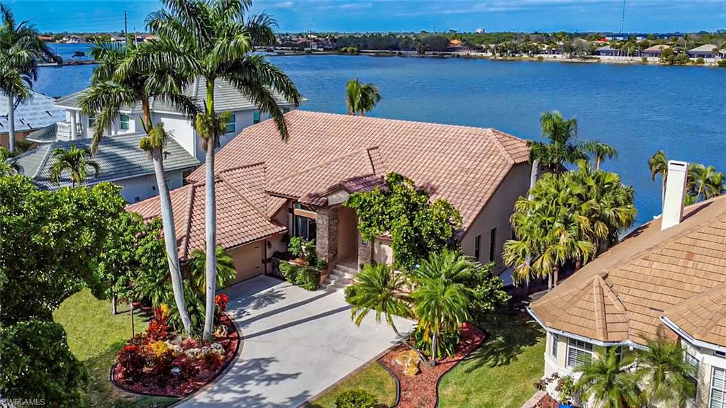 Waterfront residence featuring a barrel tile roof, arched entryway with decorative columns, and mature palm landscaping