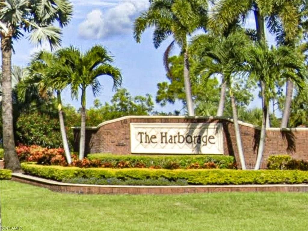 Brick masonry entrance sign with "The Harborage" script lettering, bordered by mature palm trees and manicured shrubbery