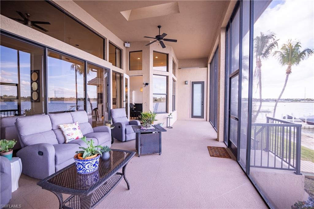 Spacious screened lanai featuring extensive glass sliding doors, water frontage, dual ceiling fans, and a balcony with metal railings