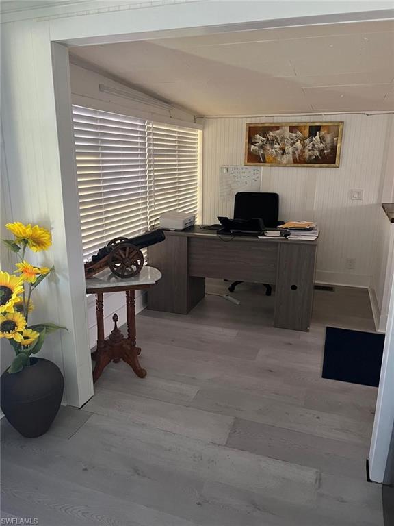 Dedicated office space featuring light wood-finish flooring, white paneling on walls, and window treatments