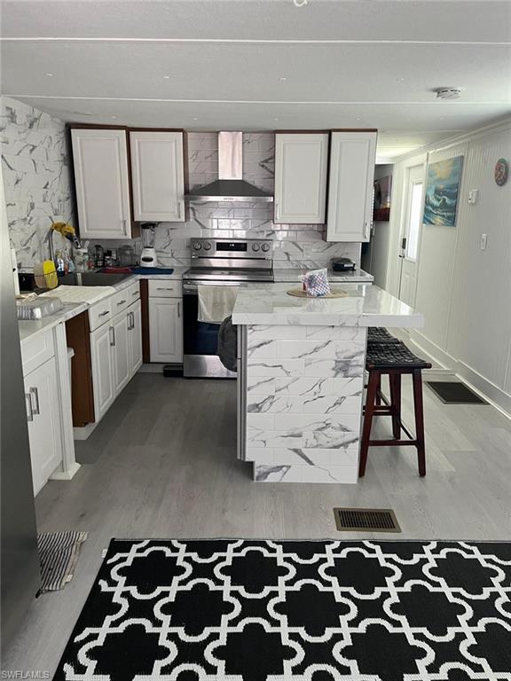 Kitchen featuring white shaker cabinetry, an island with seating, stainless steel appliances, a subway tile backsplash, and light wood-finish flooring