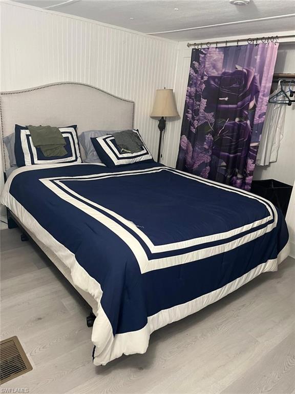 Bedroom featuring white vertical paneling, light wood-finish flooring, and a built-in closet area