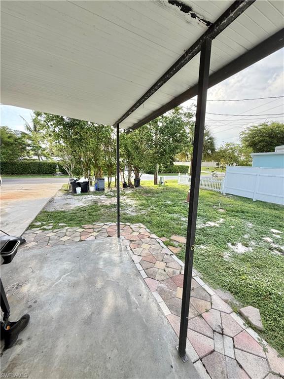 Covered patio featuring a concrete slab floor, decorative paver walkway, white vinyl fence, and mature trees