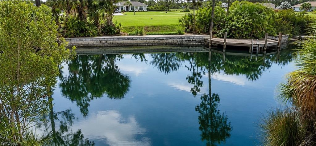 Waterfront property featuring a private wooden dock with a ladder, mature landscaping, and a manicured lawn