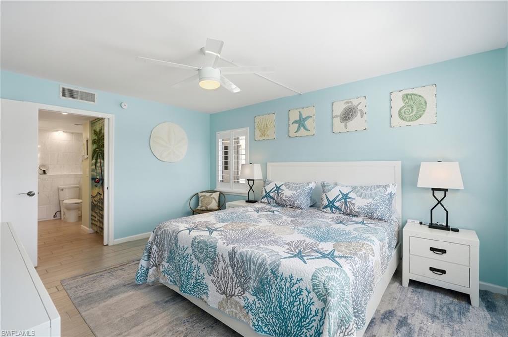 Serene primary bedroom showcasing soft turquoise walls, ceiling fan with integrated lighting, and wood-finish flooring - Virtually Edited Image