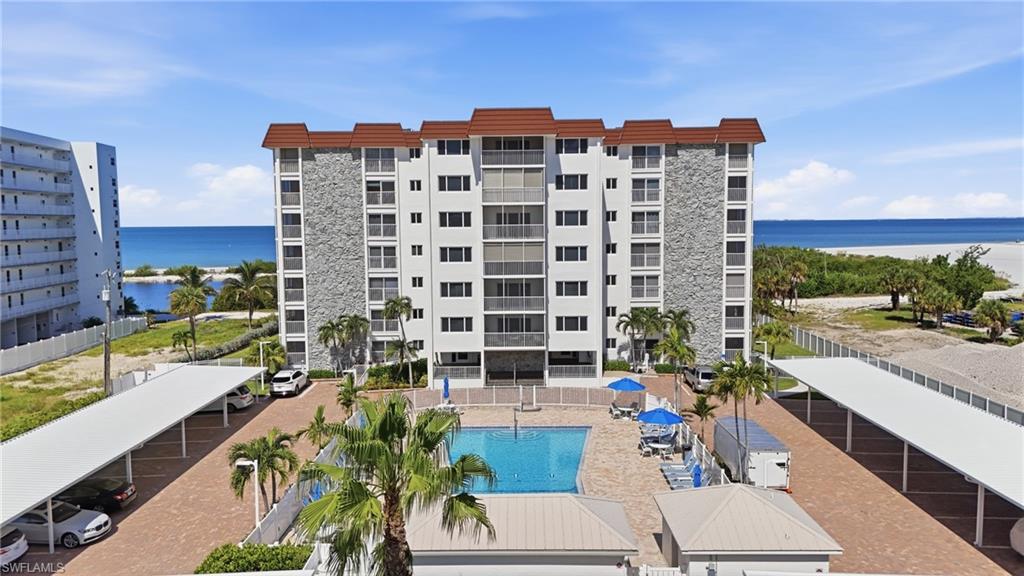 Beachfront residential complex featuring a resort-style saltwater pool with surrounding paved deck, mature palm landscaping, and direct oceanfront access - Virtually Edited Image