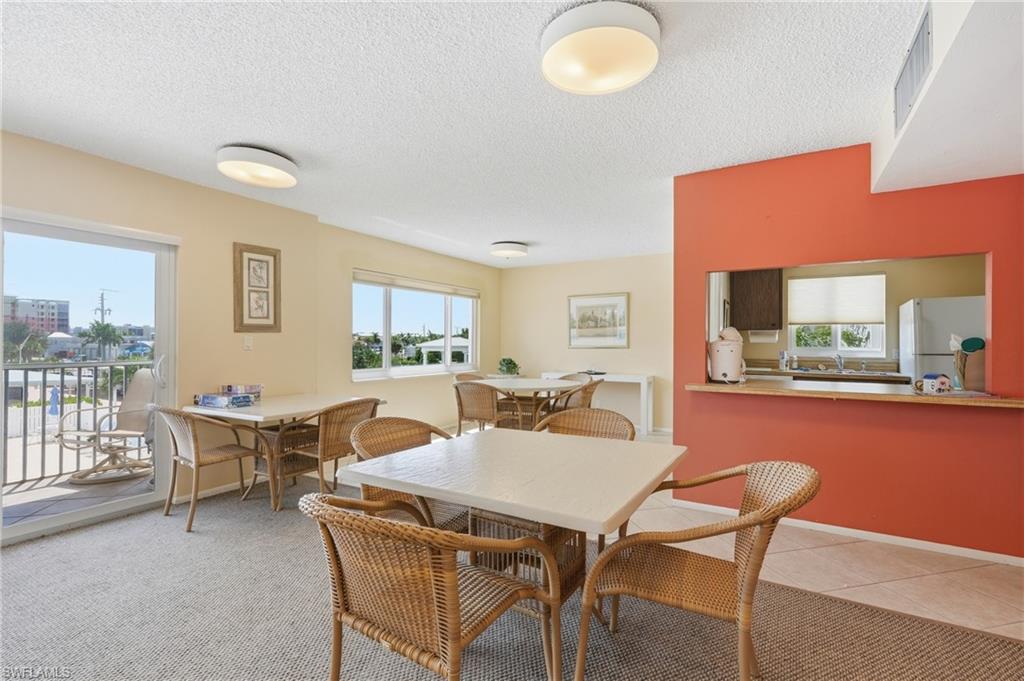 Bright, multi-use common area with expansive windows overlooking city skyline, warm neutral walls with vibrant accent wall, recessed ceiling lighting, and wood-finish flooring throughout - Virtually Edited Image