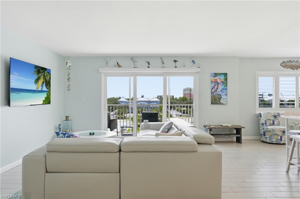 Bright, open-concept living space featuring expansive sliding glass doors that frame panoramic vistas, light wood-finish flooring throughout, and abundant natural illumination from multiple windows - Virtually Edited Image