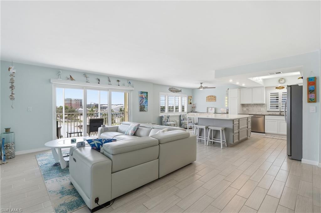 Open-concept living space featuring wood-finish flooring, a kitchen island with seating, white cabinetry, stainless steel appliances, and sliding glass doors leading to an outdoor area - Virtually Edited Image