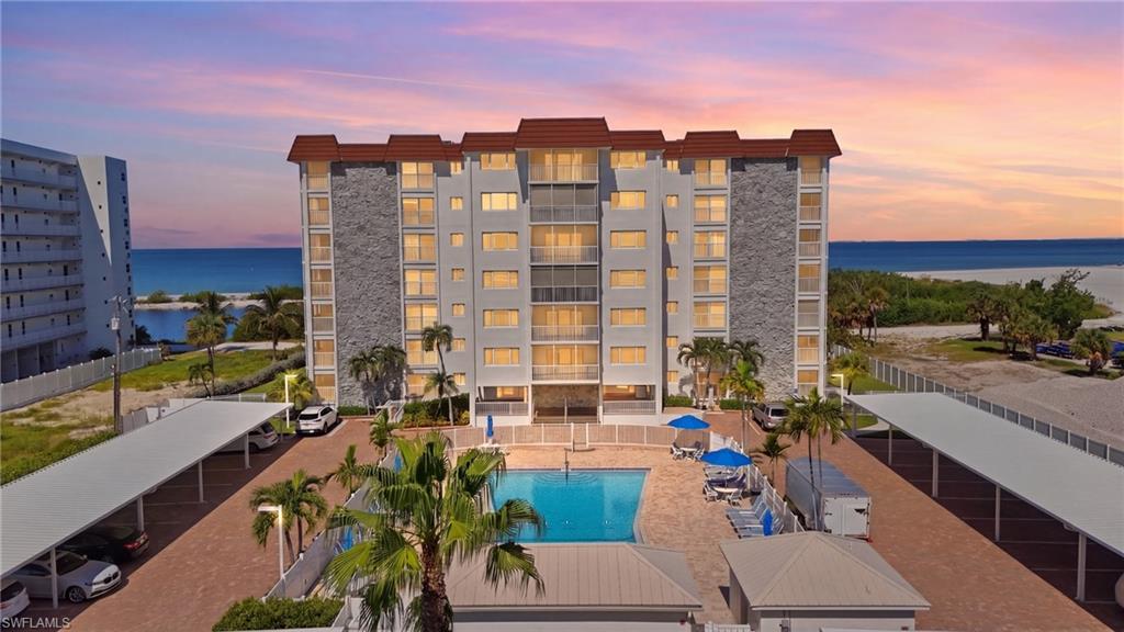 Multi-story building featuring balconies, beachfront access, a swimming pool, and covered parking - Virtually Edited Image